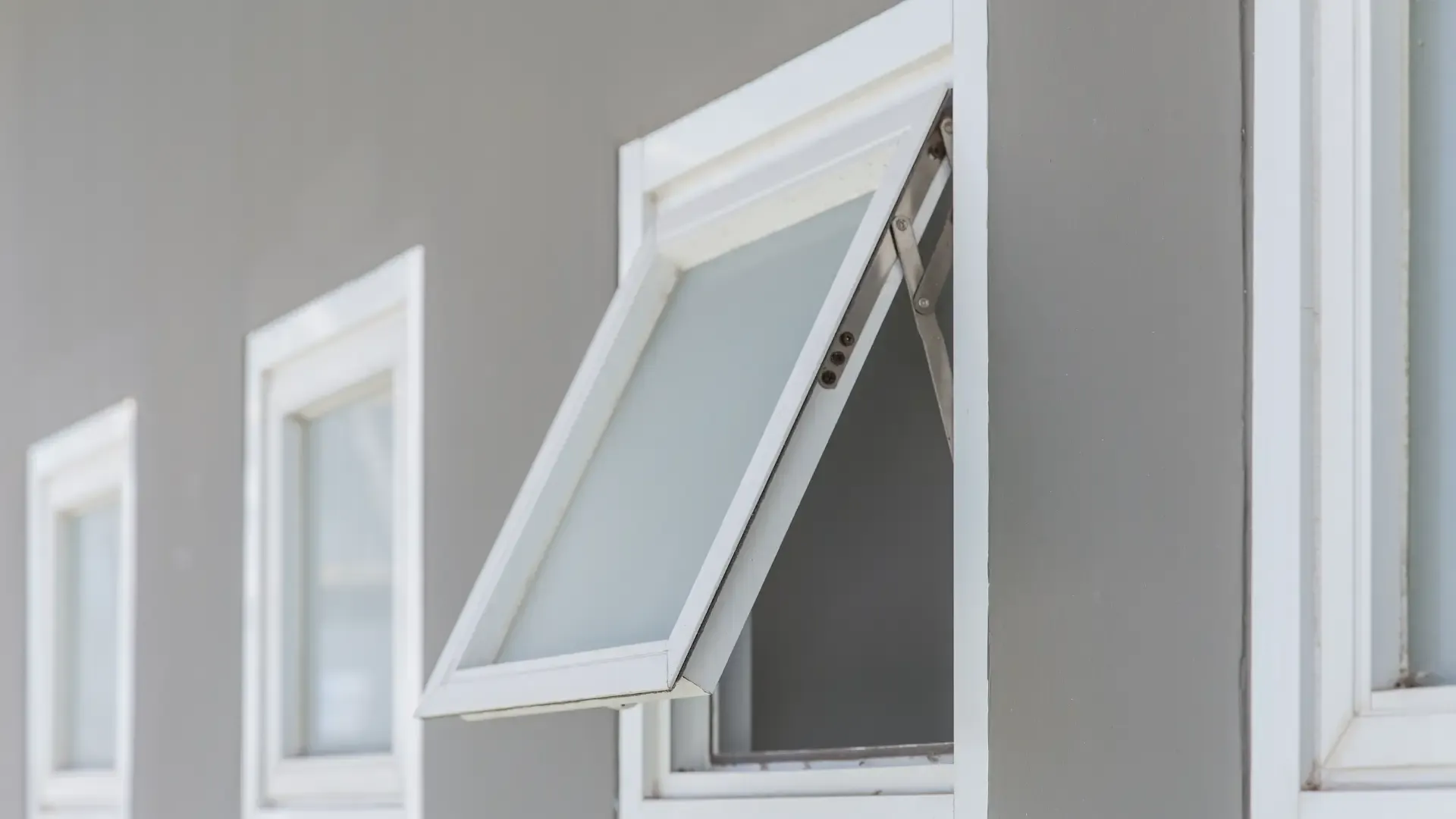 A series of three rectangular windows on a gray wall, with one window open outward. The scene conveys simplicity and minimalism.