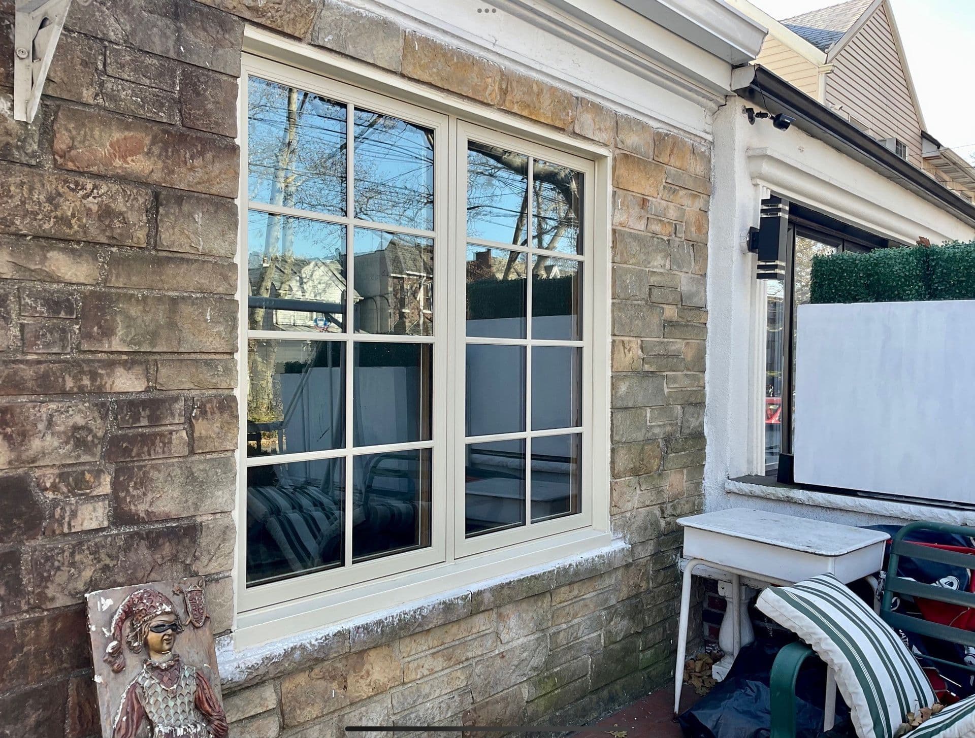 Beige double-hung window with grilles set into a stacked stone exterior wall.