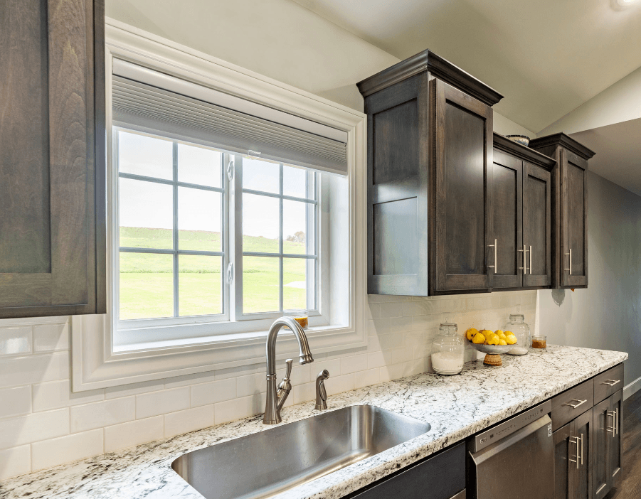 Modern kitchen with dark wood cabinets and a granite countertop. A window with a scenic view above a silver sink. Lemons and jars add a touch of color.