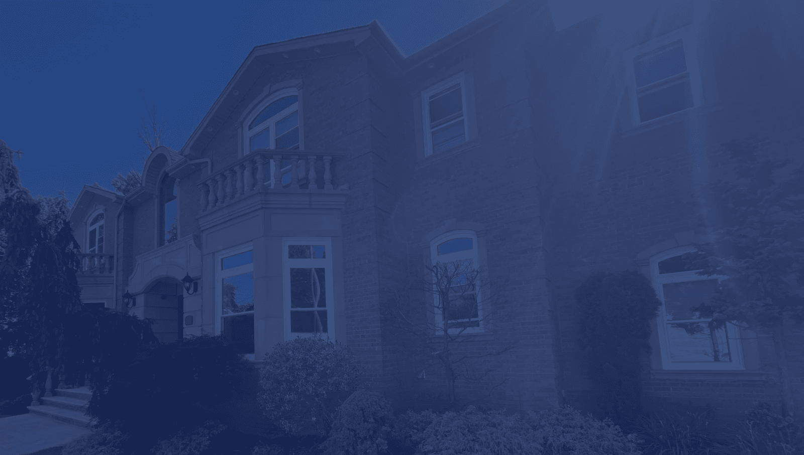 Large two-story stone home with arched windows, a small balcony, and lush green landscaping.