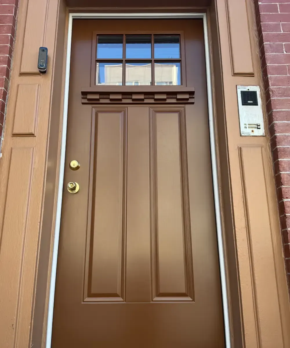 Brown front entrance door featuring a top six-lite window, brass hardware, and decorative dentil trim.