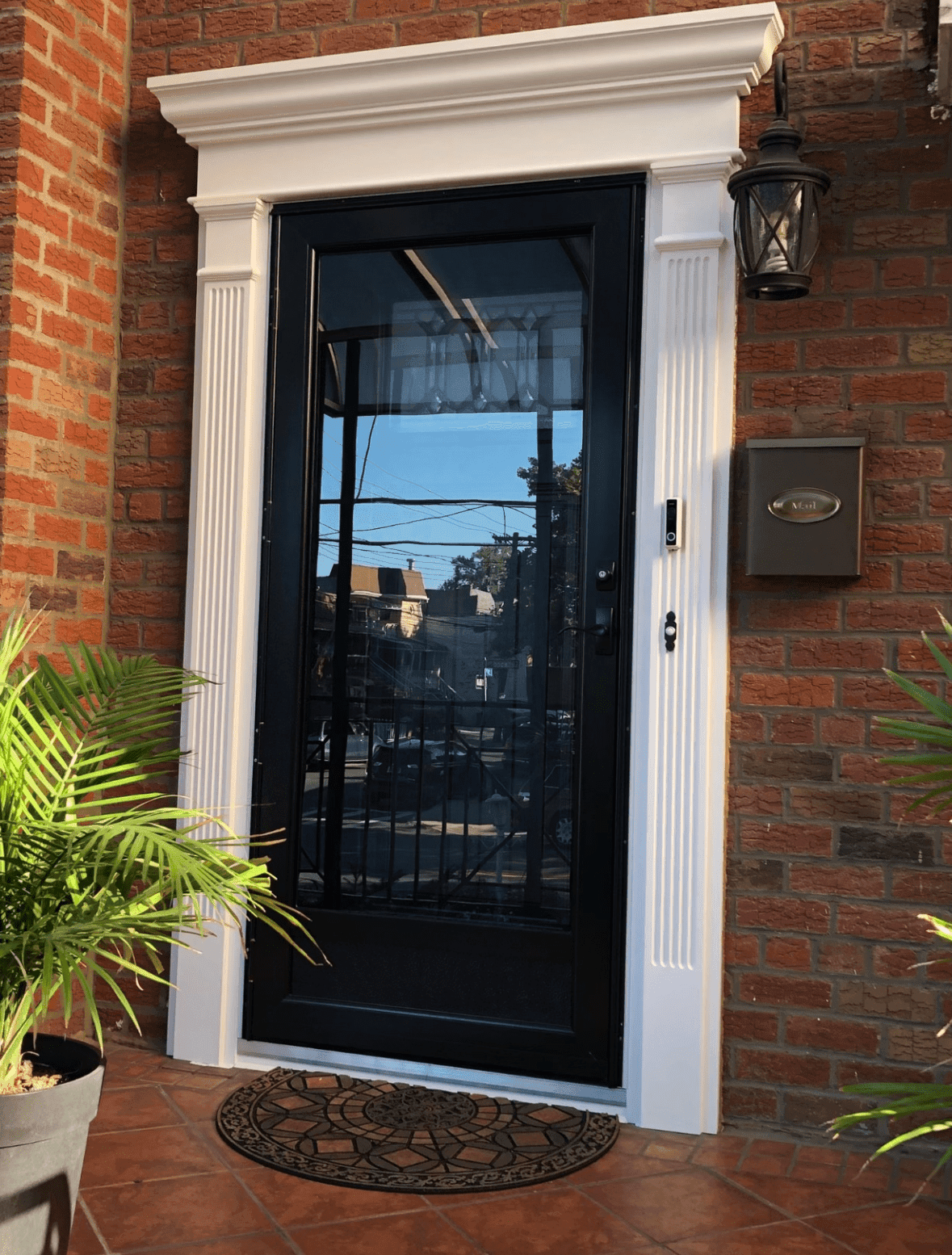 Black full-glass storm door framed by decorative white fluted molding on a red brick home.