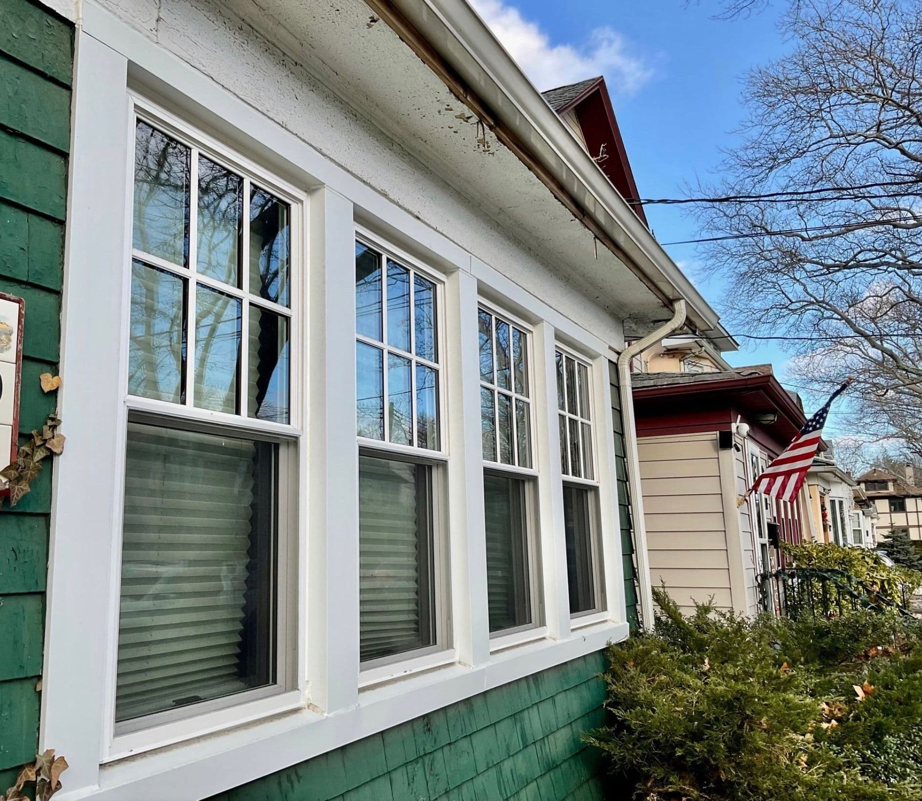 Row of white double-hung windows with top-pane grilles on a house with dark green shingle siding.