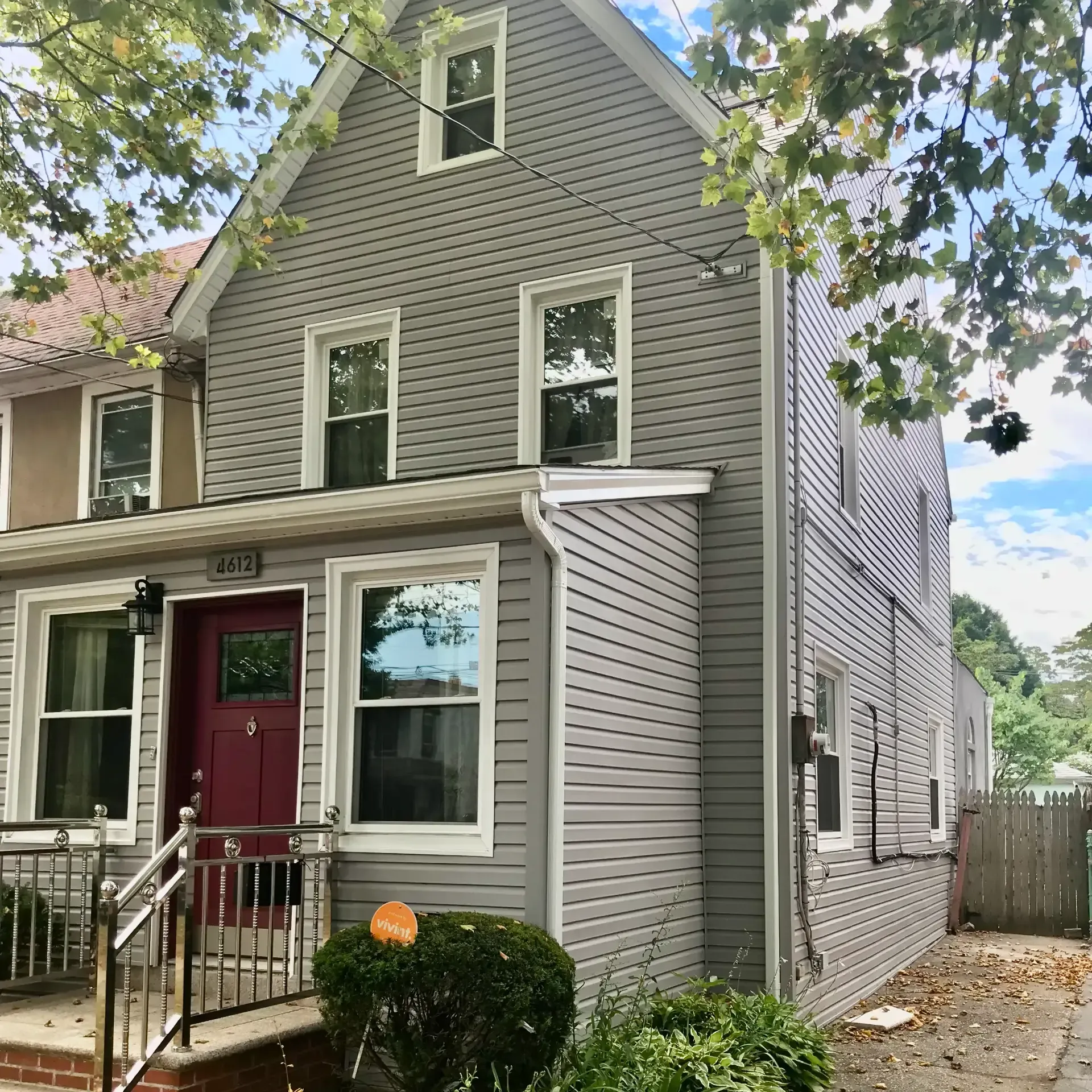 Exterior perspective of a multi-story home featuring light grey horizontal lap siding, white trim, stainless steel porch railings, and a rich maroon front door with a small window pane.