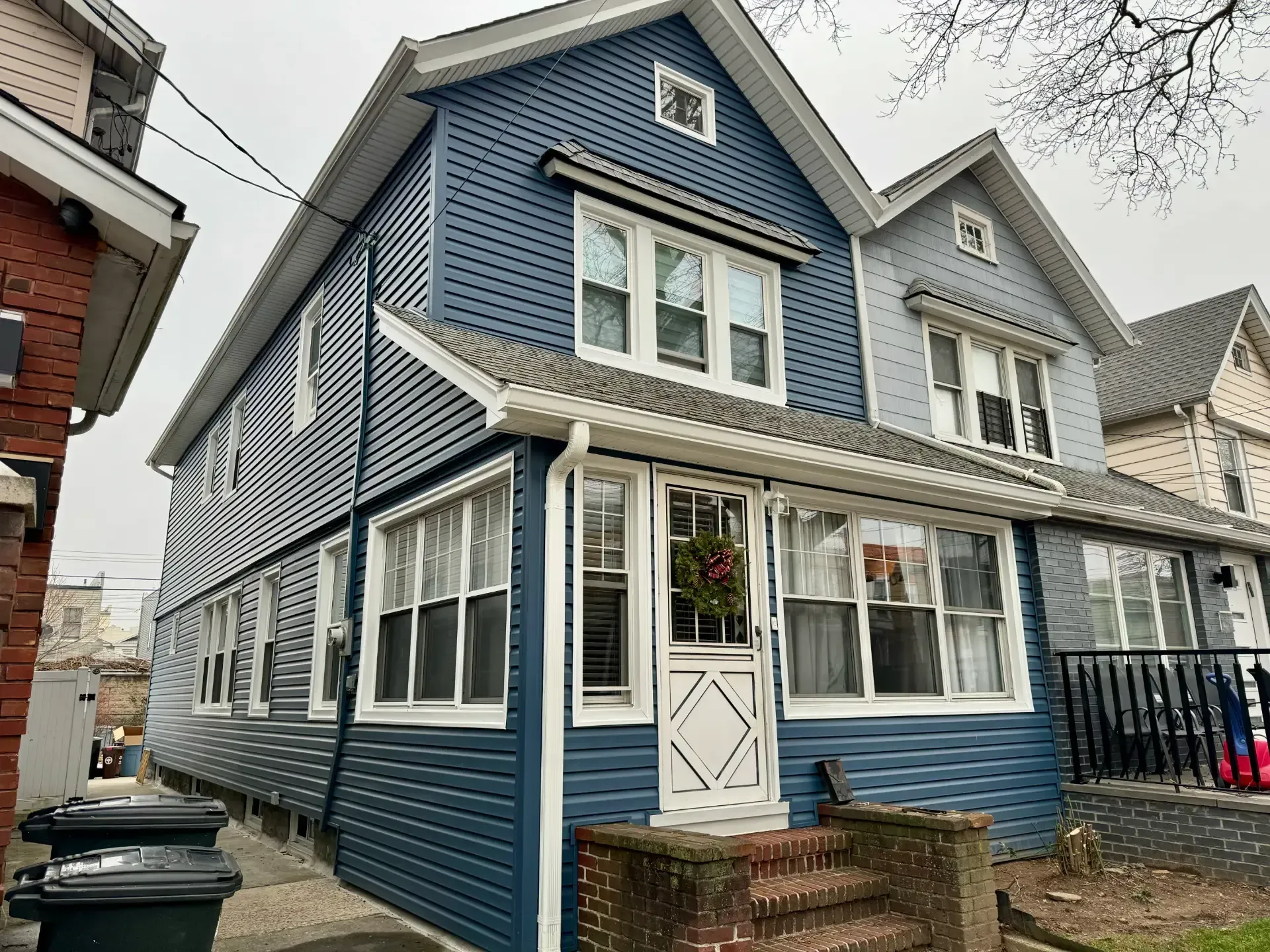 Exterior view of a multi-story home clad in slate blue horizontal lap siding, featuring bright white window trim and a white storm door set on a brick step porch.