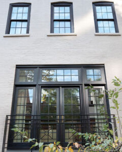 A white brick townhome with black frame double-hung windows