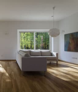 A living room with a wood floor, gray sectional, and large sliding window
