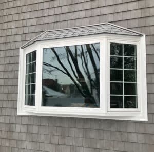 Outside view of a home that has grey shingle siding and a white framed bay window.